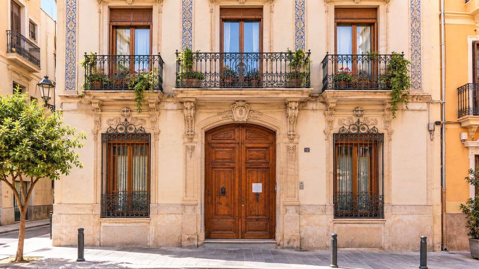Certificados Energéticos | ITE o IEE: diferencias clave y cuándo procede cada informe Una hermosa fachada de un edificio clásico español con balcones floridos, puertas de madera y detalles arquitectónicos tradicionales.